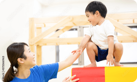 男の子が高さのある台に登りそれを支える女性職員